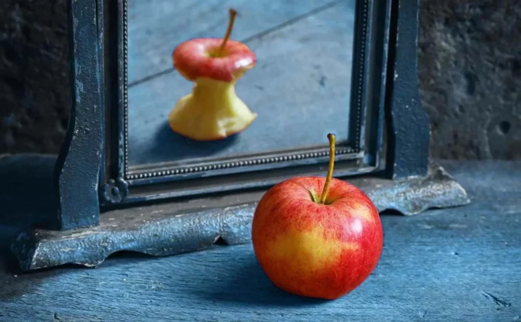 Imagen de una manzana frente a su reflejo de una manzana mordida simbolizando diferentes tipos de trastornos alimenticios.