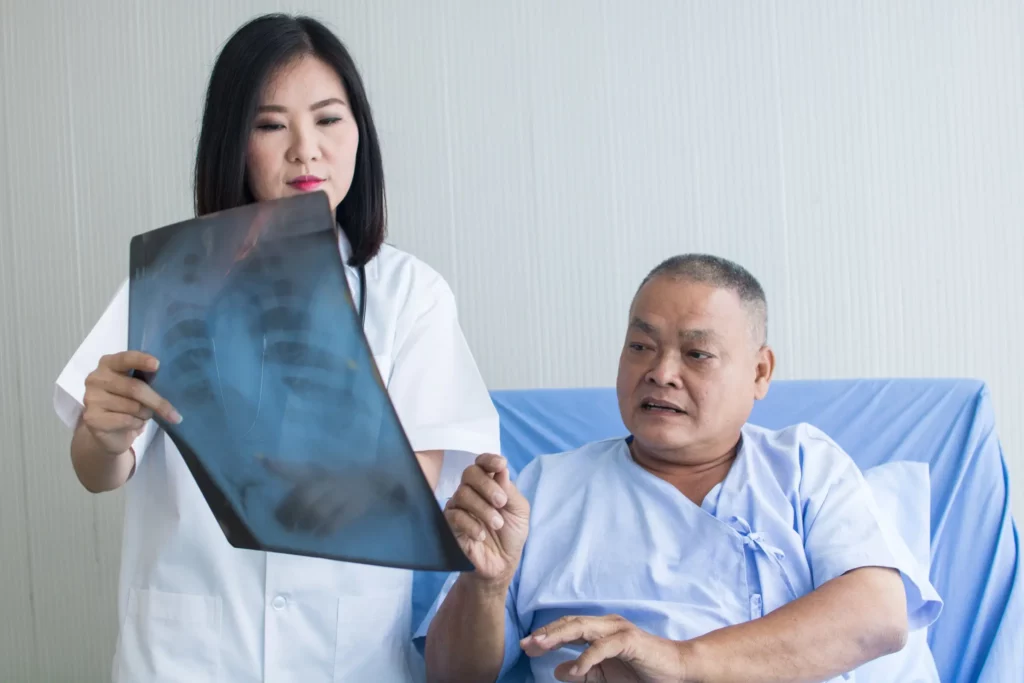 Doctora sostiene una radiografía del torso y le muestra al paciente sus resultados sobre tuberculosis