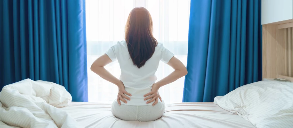 Mujer levantándose de la cama, y estirándose para evitar el dolor de espalda baja