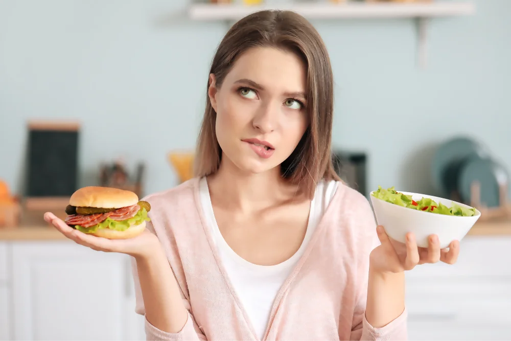 Una mujer joven se debate entre optar por una alimentación saludable con el nutricionista o darse un gusto con una hamburguesa.