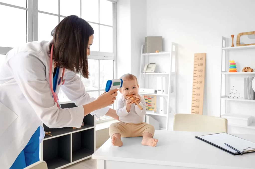 Doctora pediatra revisando la temperatura de un bebé.
