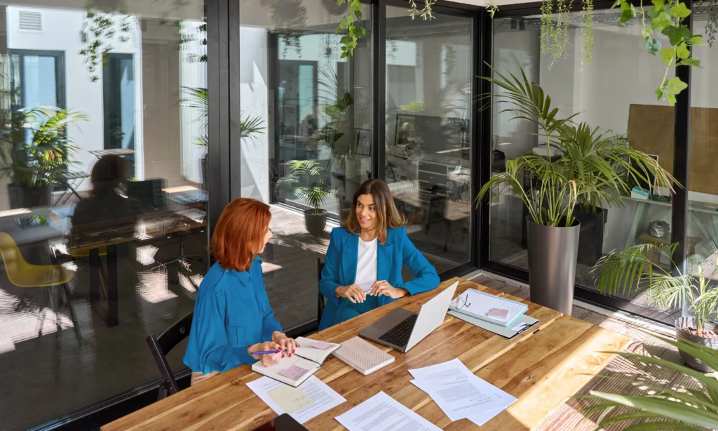 dos mujeres felices hablando en una sala de oficina con área verde alrededor 
