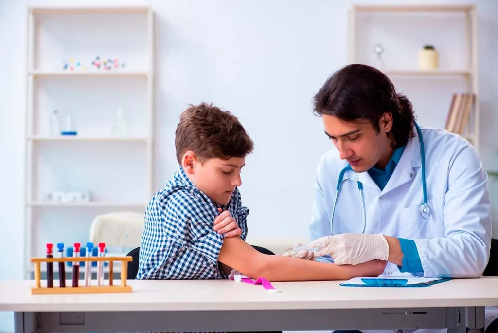 Médico tomando muestra de sangre a niño durante su consulta de hematología pediátrica.
