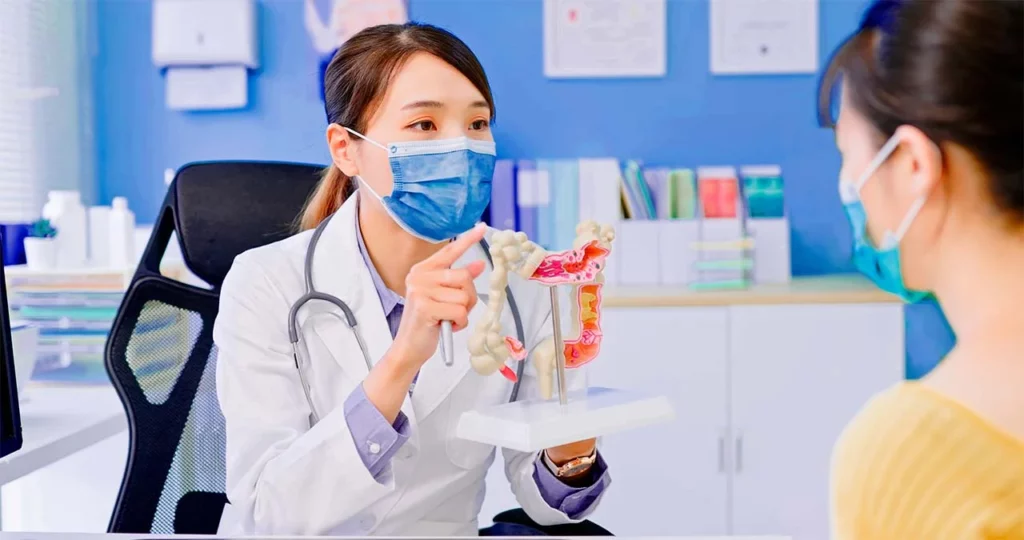 Doctora explicando a una paciente con un modelo del intestino grueso, el procedimiento de la cirugía de colon y recto.