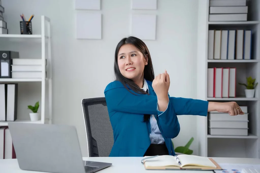 Mujer con computadora y agenda estirándose 