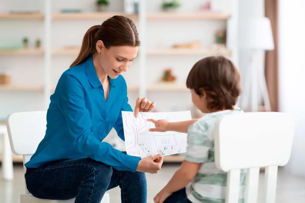 Paidopsiquiatra en consulta con niño, quien está sentado frente a ella señalando un punto en un dibujo.