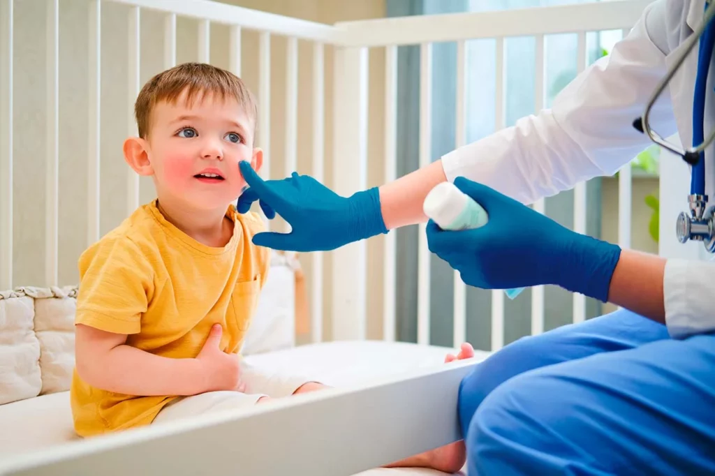 Dermatólogo pediátrico aplicando una crema en las mejillas a su paciente niño.