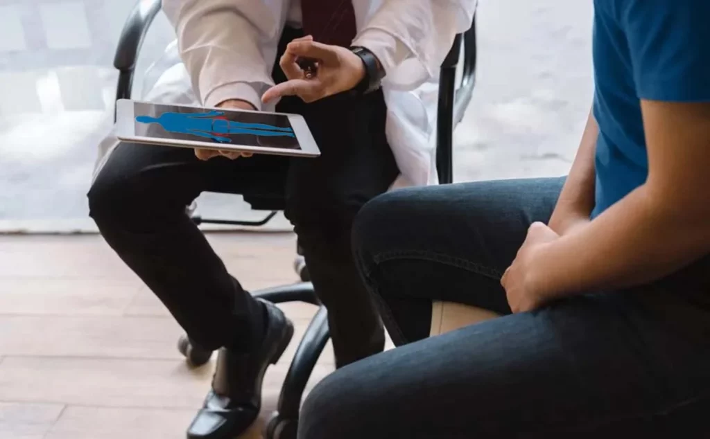 Paciente en consulta con un médico, quien le explica qué es el cáncer de testículo, con el apoyo de una Tablet.