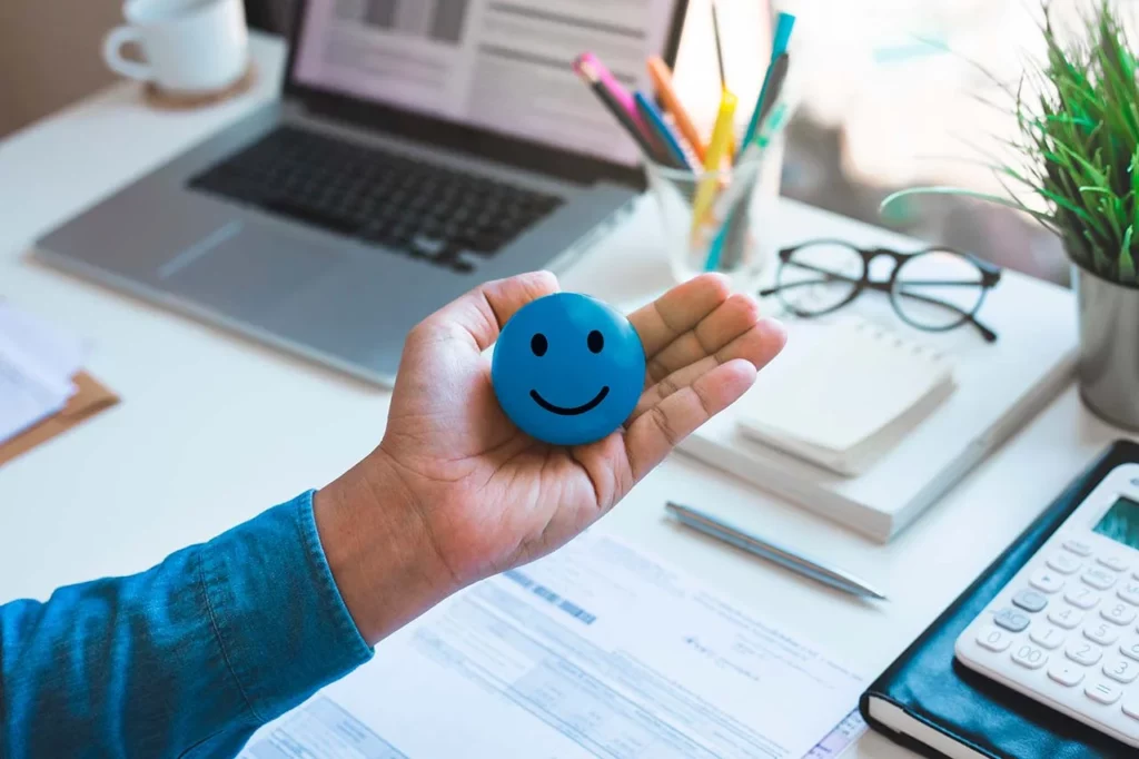 Persona sosteniendo cara feliz con cosas de escritorio de fondo