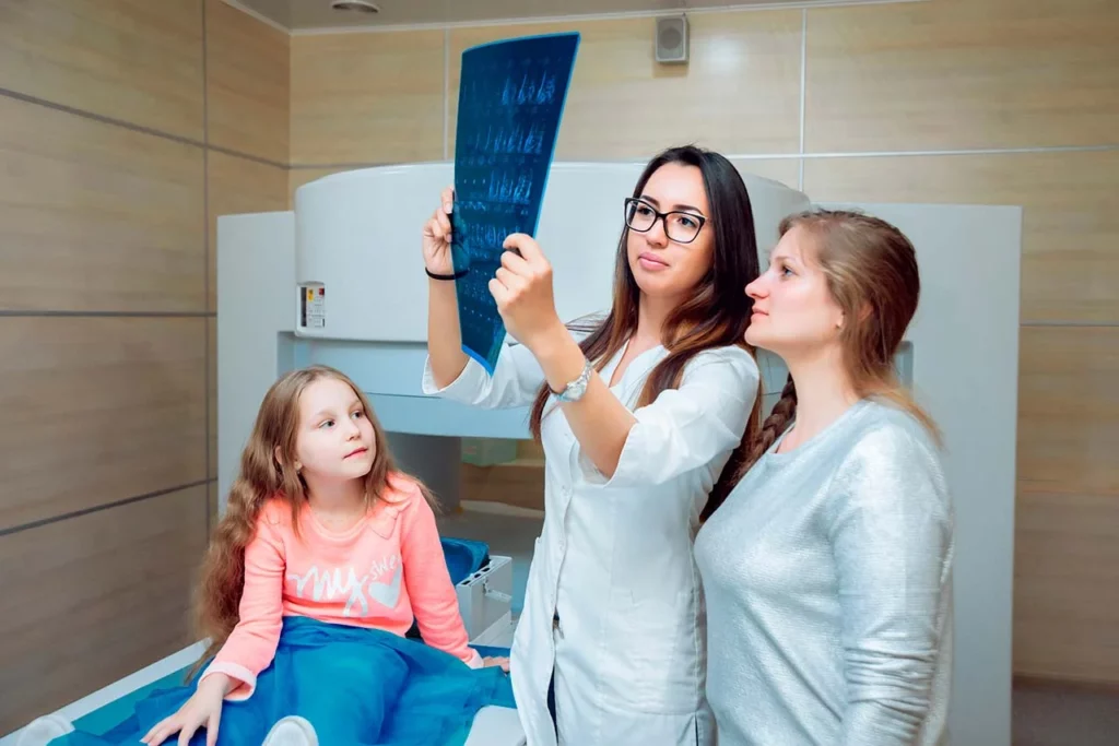 Niña, paciente de cirugía oncológica pediátrica, en consulta con su doctora, quien explica una radiografía a su madre.